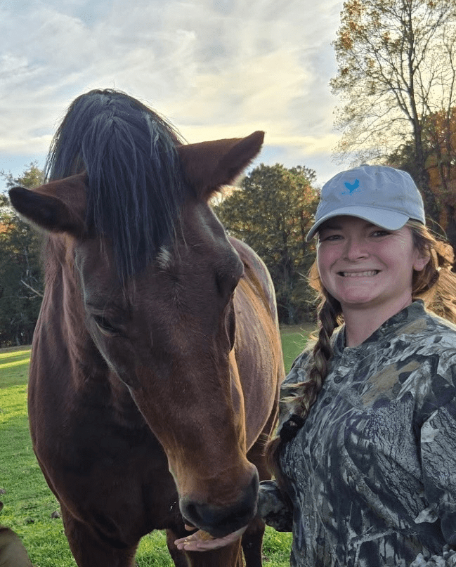 A woman smiling next to a brown horse outdoors.